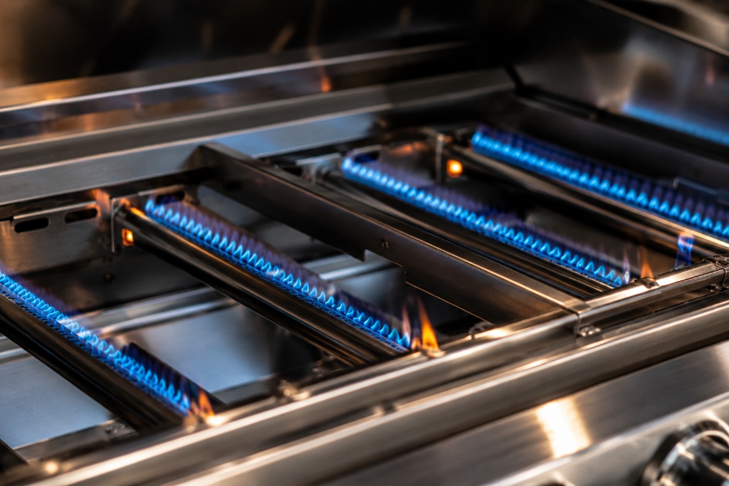 Close-up of clean blue gas grill burner flames and stainless burner components after performance inspection